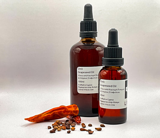 Two bottles of chili grapeseed oil with a dried chili pepper and seeds on a white background
