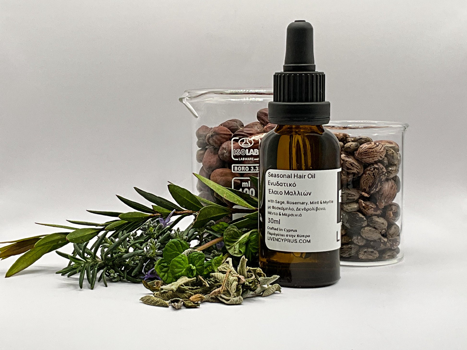 Bottle of hair oil with dropper, jar of herbs, and green leaves on a white background