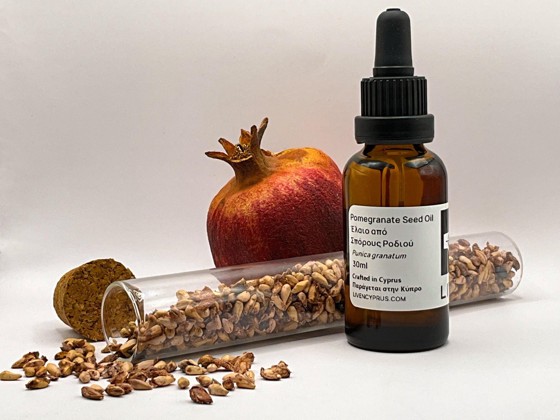 Bottle of pomegranate seed oil with pomegranate and seeds on a white background