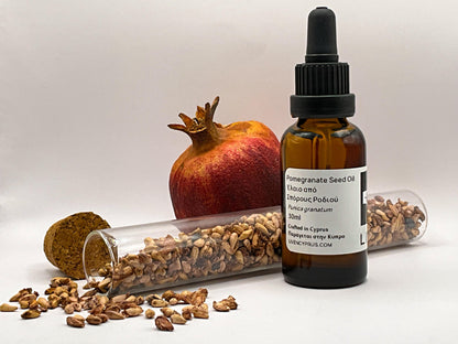 Bottle of pomegranate seed oil with pomegranate and seeds on a white background