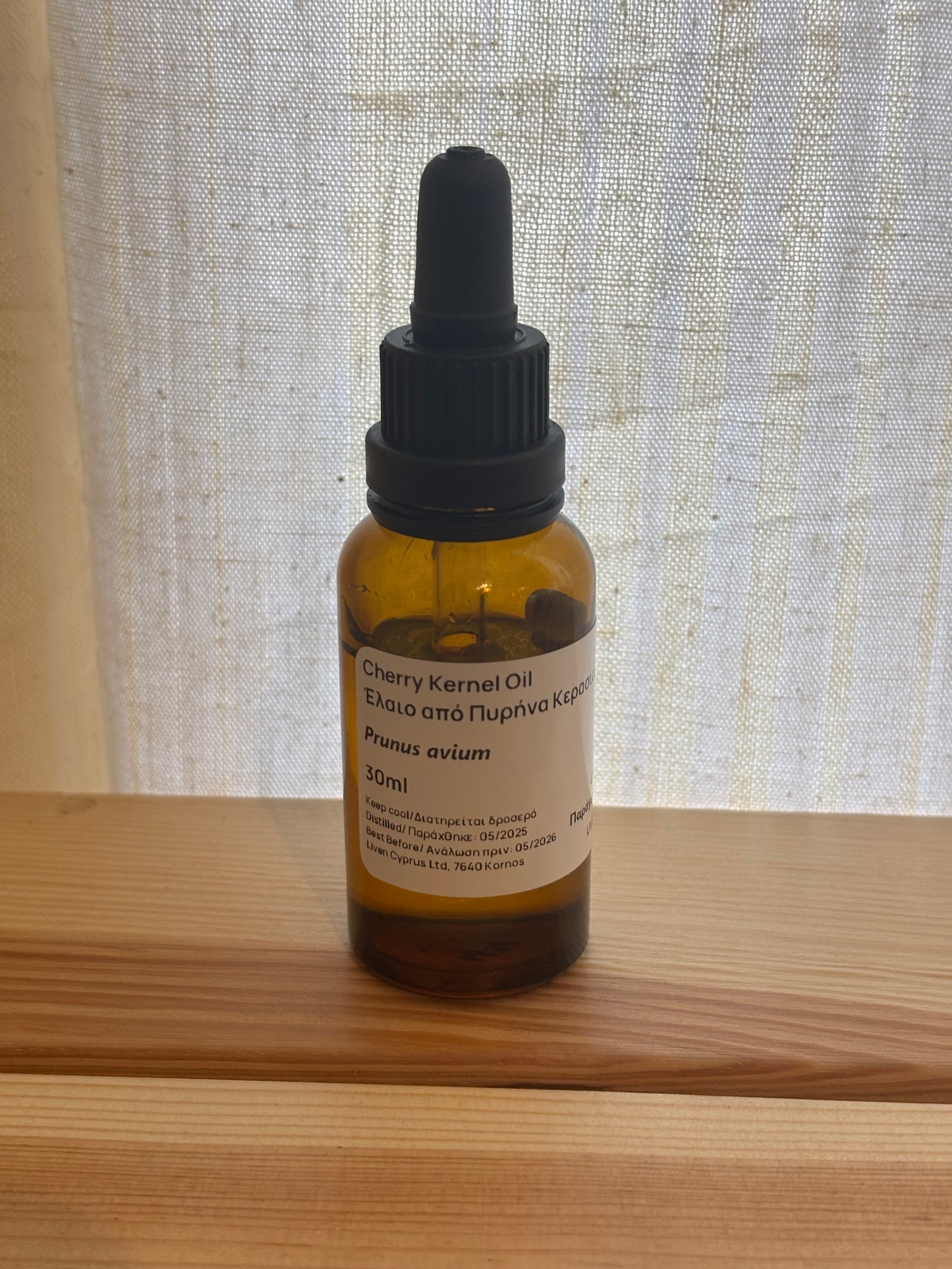 Bottle of cold-pressed cherry kernel oil with a dropper on a wooden surface