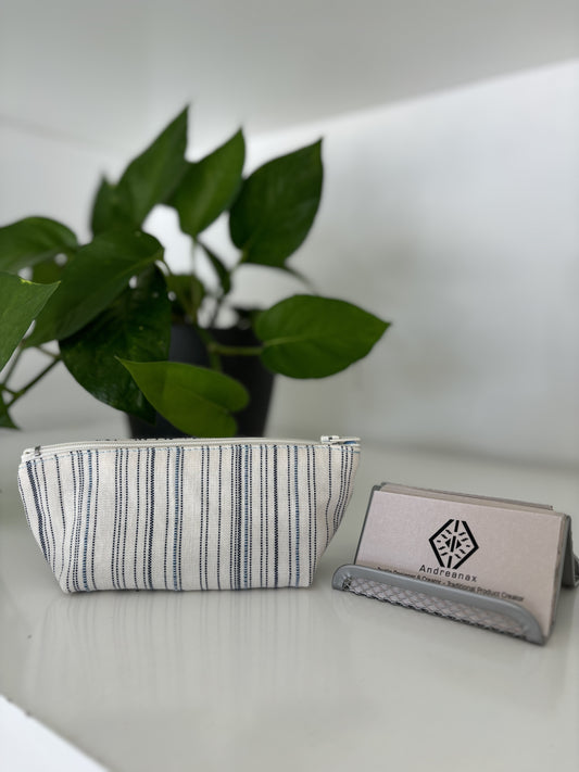 A custom made cotton gift bag with a striped pattern in white and blue, displayed next to a small plant, placed on a white surface.