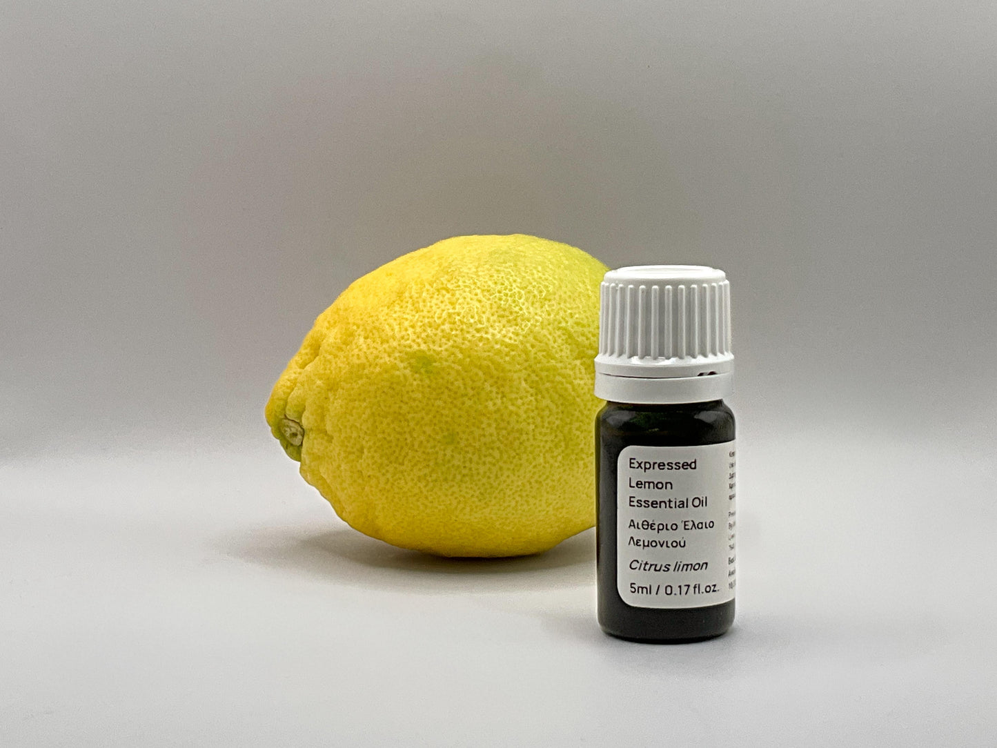 Lemon and a bottle of expressed lemon essential oil on a gray background